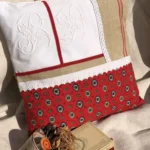 Duo de coussins décoratifs en toile provençale rouge à motifs type mouche coloré. Ornements de linge ancien blanc, monogramme, dentelle, et toile de torchon en jute naturelle